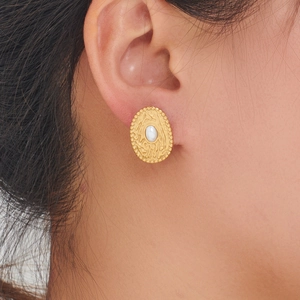Macro side view of vintage oval gold earrings with pearl inlay and embossed textures