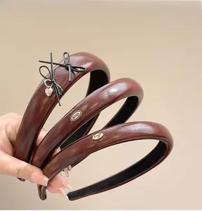 Close-up of three premium burgundy PU leather headbands with metallic charms and bow detail