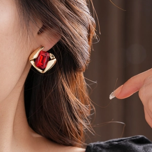 Close-up of model wearing gold-rimmed red rectangular gemstone earring with fluid metal design