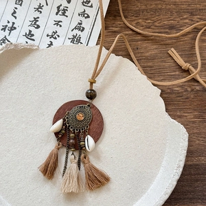 Detail of bohemian wooden pendant with layered bronze filigree, tassel and natural seashell