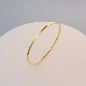 Polished 18K gold plated titanium steel slim bangle on a minimalist round display stand