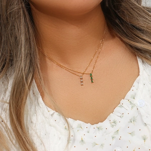 Close-up of layered gold necklaces with sparkling white and green teardrop pendants