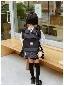 Detail of black kids backpack with cat patch and plush bread pendant in outdoor setting