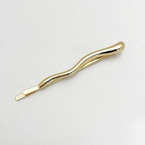Close-up of wavy golden alloy hair clip with polished metallic texture on white background