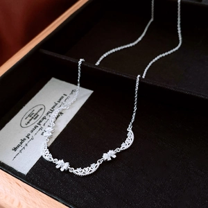 Detailed close-up of a silver bow necklace with intricate floral patterns and small crystals