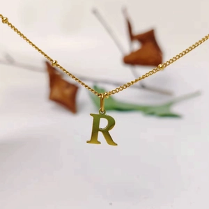 Macro detail of a gold-toned letter R pendant dangling from a delicate titanium steel bead chain