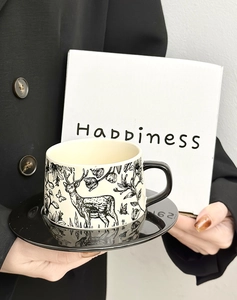 Detail of cream ceramic coffee cup with deer patterns and black saucer in gift packaging