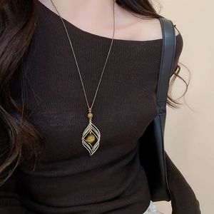 Detail of leaf-shaped pendant necklace with amber stone on a model in brown clothes