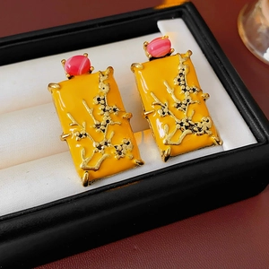 Détail macro de boucles d'oreilles en émail jaune avec relief floral doré et gemme rose