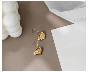 Detail of elegant gold heart dangle earrings on a beige leather and silk display