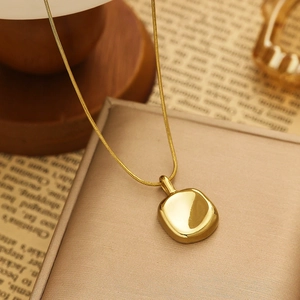 Detail of a polished gold square pendant necklace resting on a beige leather jewelry box