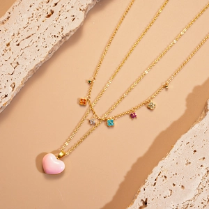 Detail of layered gold necklace with pink heart pendant and colorful gemstone accents