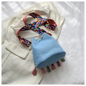 Close-up of ethnic canvas bucket bag with colorful woven strap and hanging fringe tassels