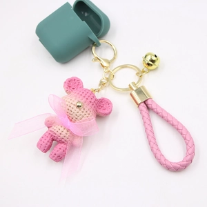 Green silicone AirPods case with pink woven bear keychain and golden bell attachment