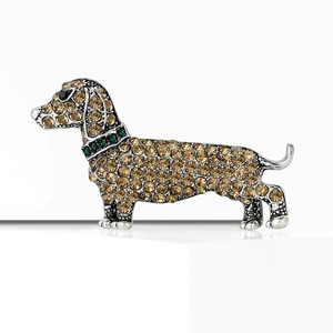Sparkling dachshund brooch with silver metal base and golden crystals on white stand