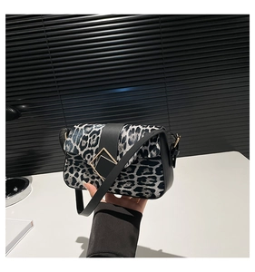 Close-up of black and white leopard print bag with black leather strap and gold buckle