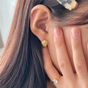 Detail of golden shell earrings and a rectangular zircon ring worn for a refined look