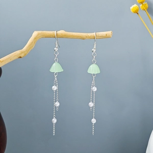 Detail of silver long tassel earrings with green flower buds and white pearls on wood branch