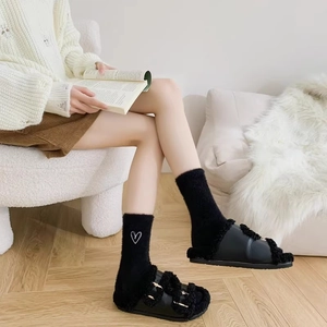 Detail of plush black slippers with metal buckles and heart embroidered fleece socks