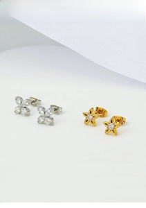 Detailed shot of sparkling marquise zircon clover and golden star studs on white fabric