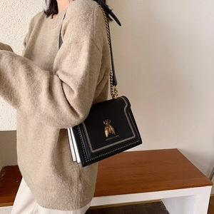 Chic black leather flap bag with gold bee buckle and chain strap on female model
