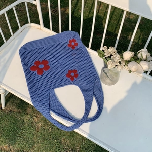 Detail der blauen Stricktasche mit roten Blumenmustern auf einer weißen Vintage-Bank