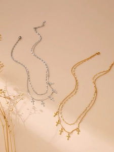 Detail of layered gold and silver cross necklaces with mixed chain textures on beige