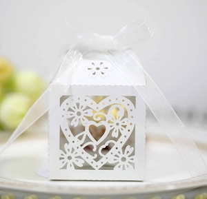 Detail of white laser-cut heart favor box with elegant sheer ribbon on a ceramic plate