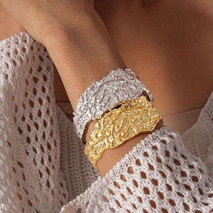 Close-up of chunky gold and silver lava texture bangles worn over a beige knit sweater