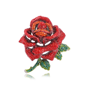 Vintage rose brooch with red rhinestones and blue leaves on a white background