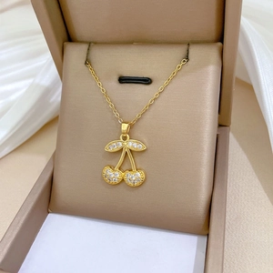Close-up of gold cherry pendant necklace with pavé zircon stones in a jewelry box