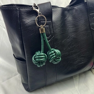 Detail showing a dark green leather monkey fist knot keychain on a black tote bag