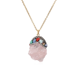 Macro shot of pink raw stone pendant with colorful crystals and gold chain details