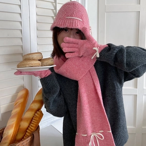 Three-piece pink knit winter set featuring scarf, hat, and gloves with white bow accents