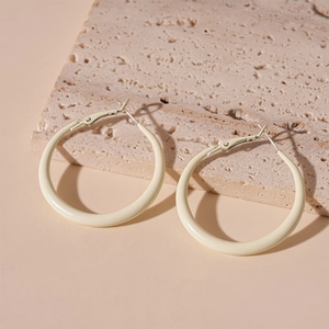 Detail of beige resin hoop earrings on a textured stone surface with soft lighting