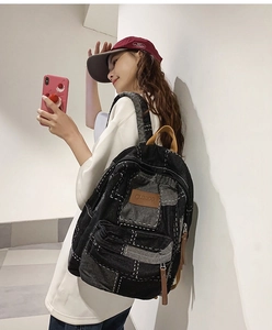 Model wearing a vintage black denim backpack with white stitching and leather detail
