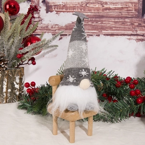 Close-up of knit Christmas gnome with snowflake hat sitting on a small wooden chair