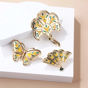 Elegant gold butterfly and fan enamel brooches displayed on a white podium