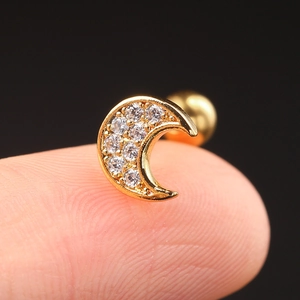 Macro shot of a gold crescent moon stud earring with white zircons on a fingertip