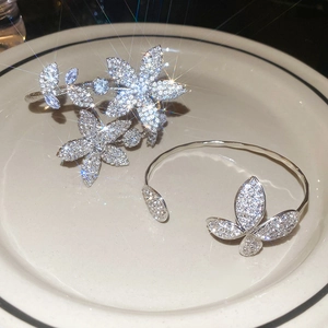 Detail of silver floral and butterfly open bangles with pavé diamonds on a white plate