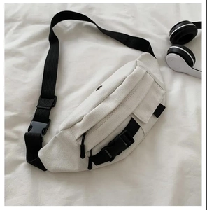 Detailed view of white canvas chest bag with black straps and buckles on a fabric background