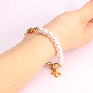 Close-up of pearl and gold chain bracelet featuring a polished letter B pendant