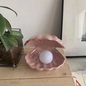 Detailed view of pink ceramic shell lamp with pearl light bulb on a wooden shelf