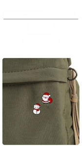 Detail of Santa Claus and Snowman enamel pins pinned onto a dark green canvas bag