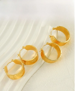 Détail de boucles d'oreilles créoles dorées avec texture martelée et reflets ondulés