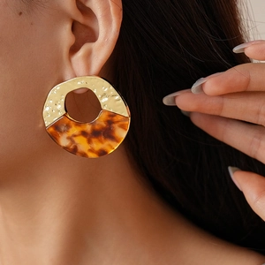 Detail of golden metal and tortoiseshell acrylic earrings worn by a female model