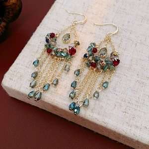 Detailed close-up of golden tassel earrings with red and green crystals on linen background
