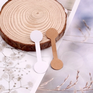 Dumbbell-shaped jewelry price tags in white and kraft paper colors on a wooden base