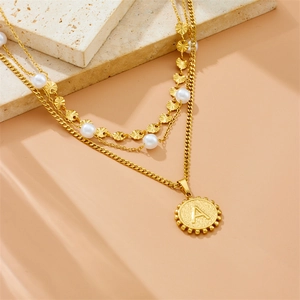 Three-layer gold necklace with white pearls and round letter A pendant on stone