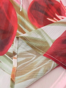 Vue macro du tissu en mousseline légère avec imprimé floral rouge et vert et couture précise